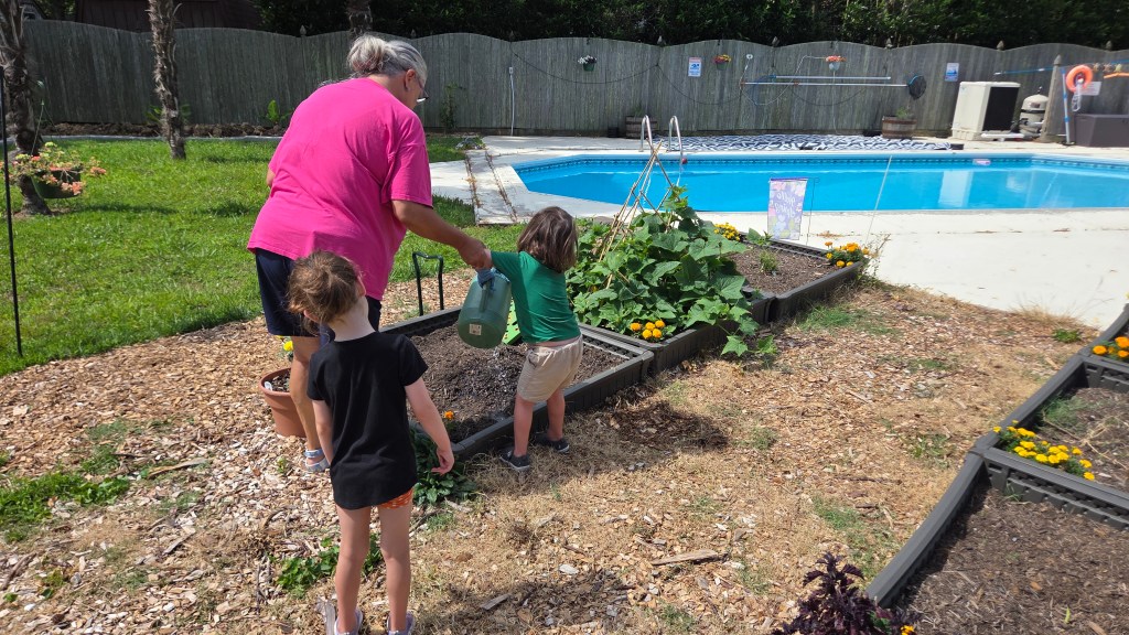 An adult woman and two children tending to a vegetable garden next to a swimming pool, with the woman watering plants while the children observe.